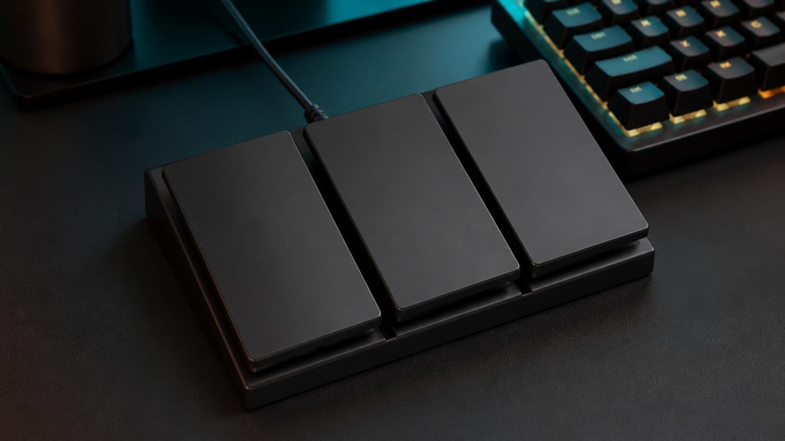 A three-pedal USB foot switch on a desk next to a mechanical keyboard